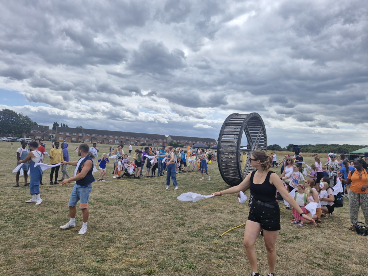 Performers dance around a giant wooden wheel at the Chadwell Big Lunch